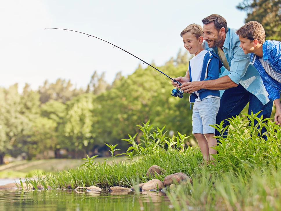 Dad fishing with two happy young sons by the river