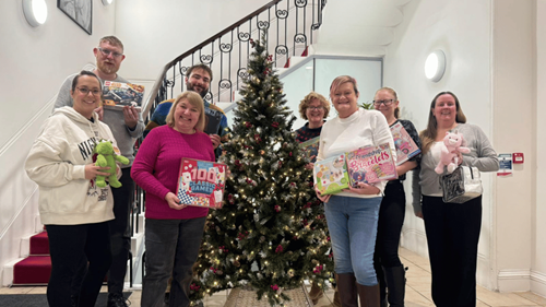 Unity Mutual team in front of the Christmas tree holding presents for the Wood Street Mission